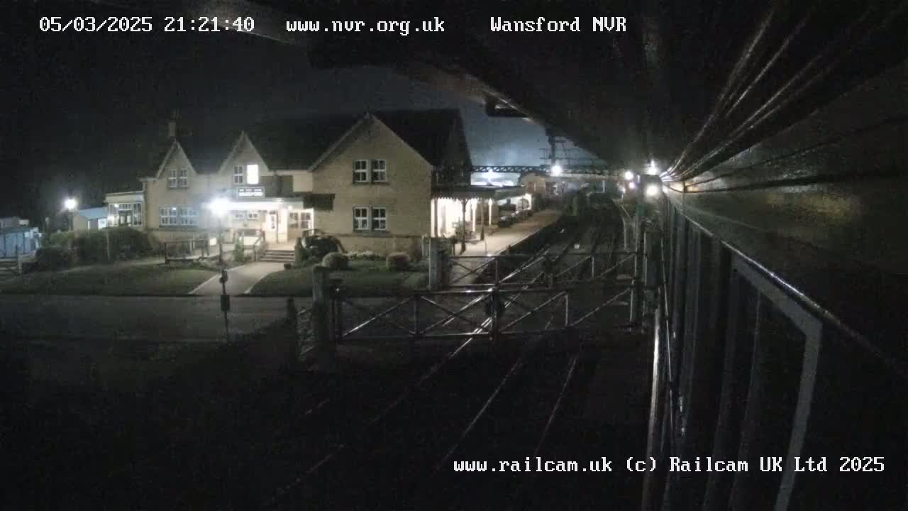 A nighttime view of a train station building and railway tracks under dark skies.