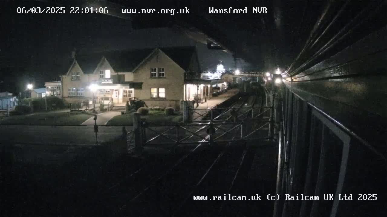 A nighttime view from a train shows a dimly lit train station with a building and tracks.