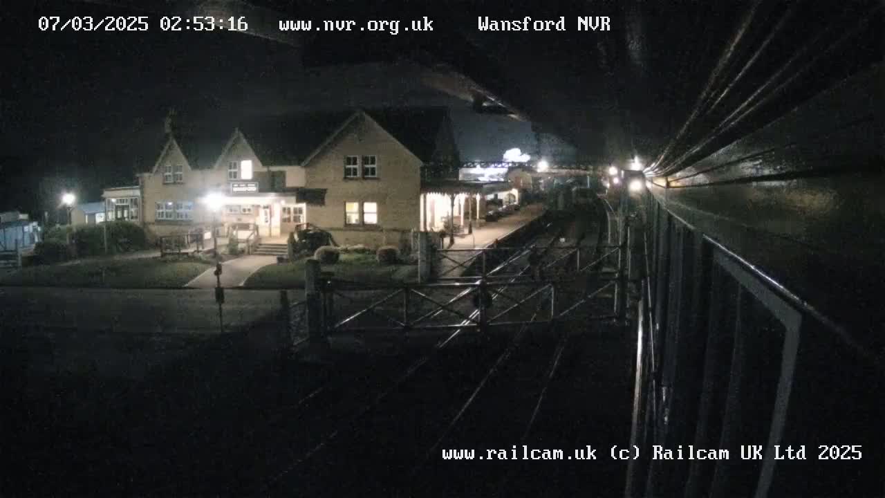 A nighttime view from a train shows a station building and tracks under a dark sky.