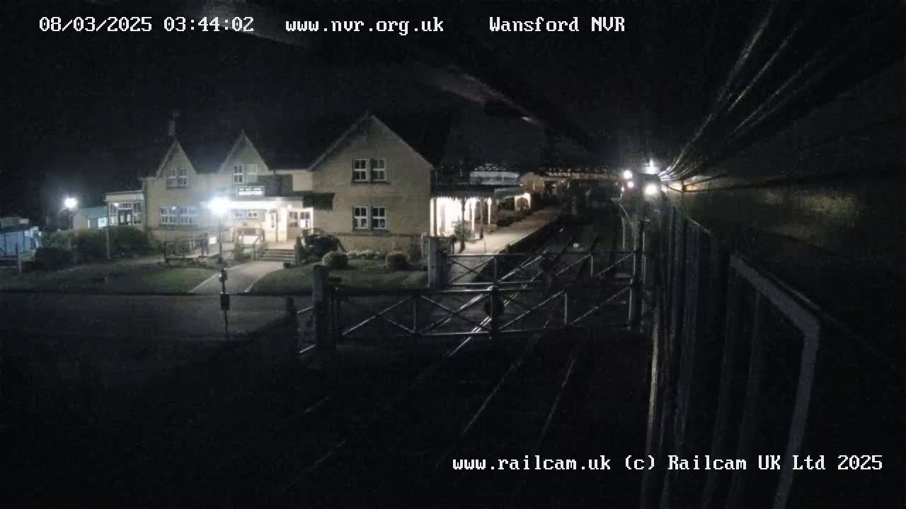 A nighttime view of a train approaching a station building, under dark skies.