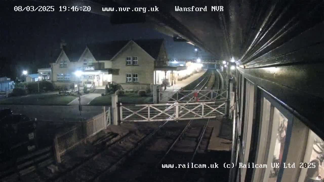 A nighttime view from a train of a station building and level crossing gates, with a clear sky.