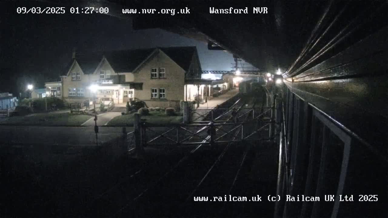 A nighttime view from a train shows a station building and tracks.