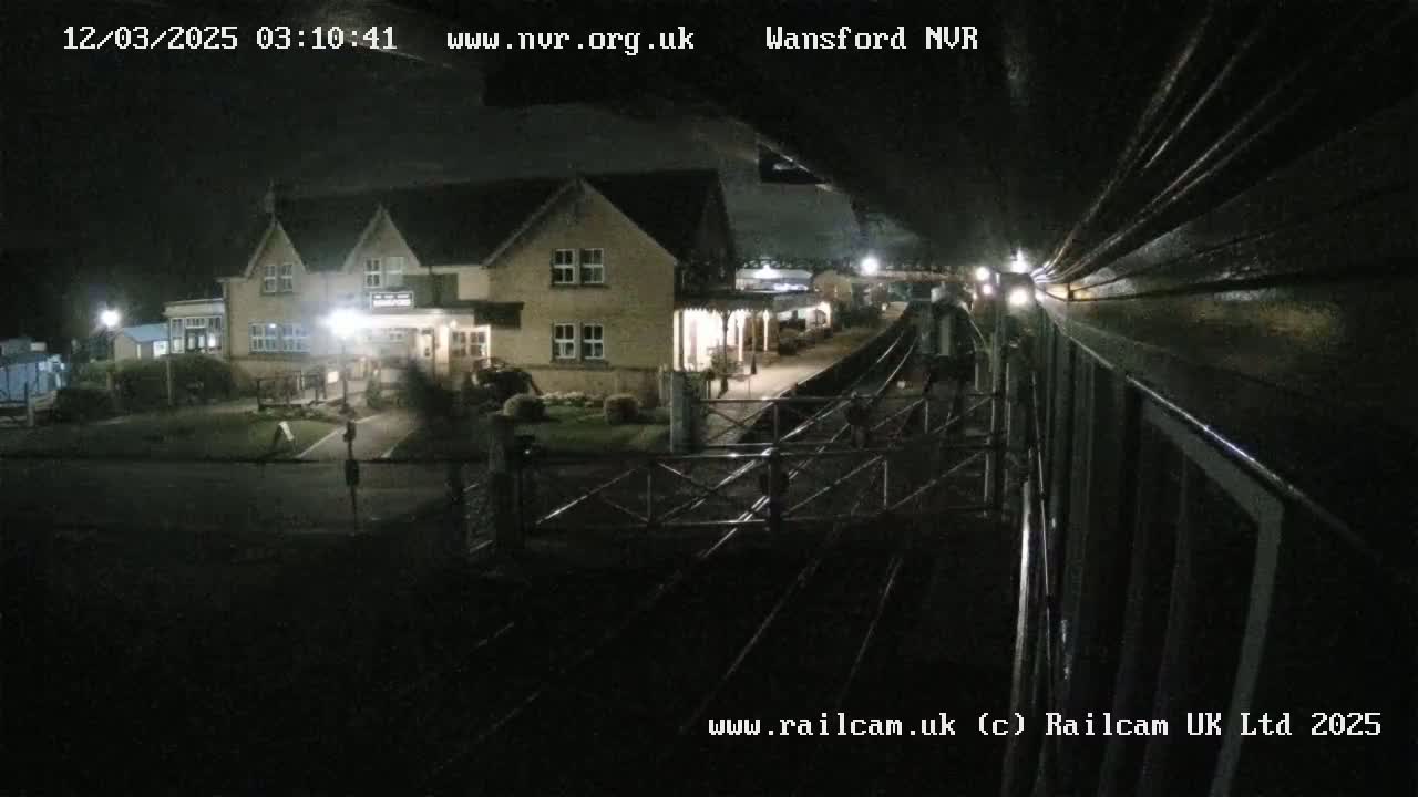 A nighttime view from a train shows a two-story building with lights on near a railway station.