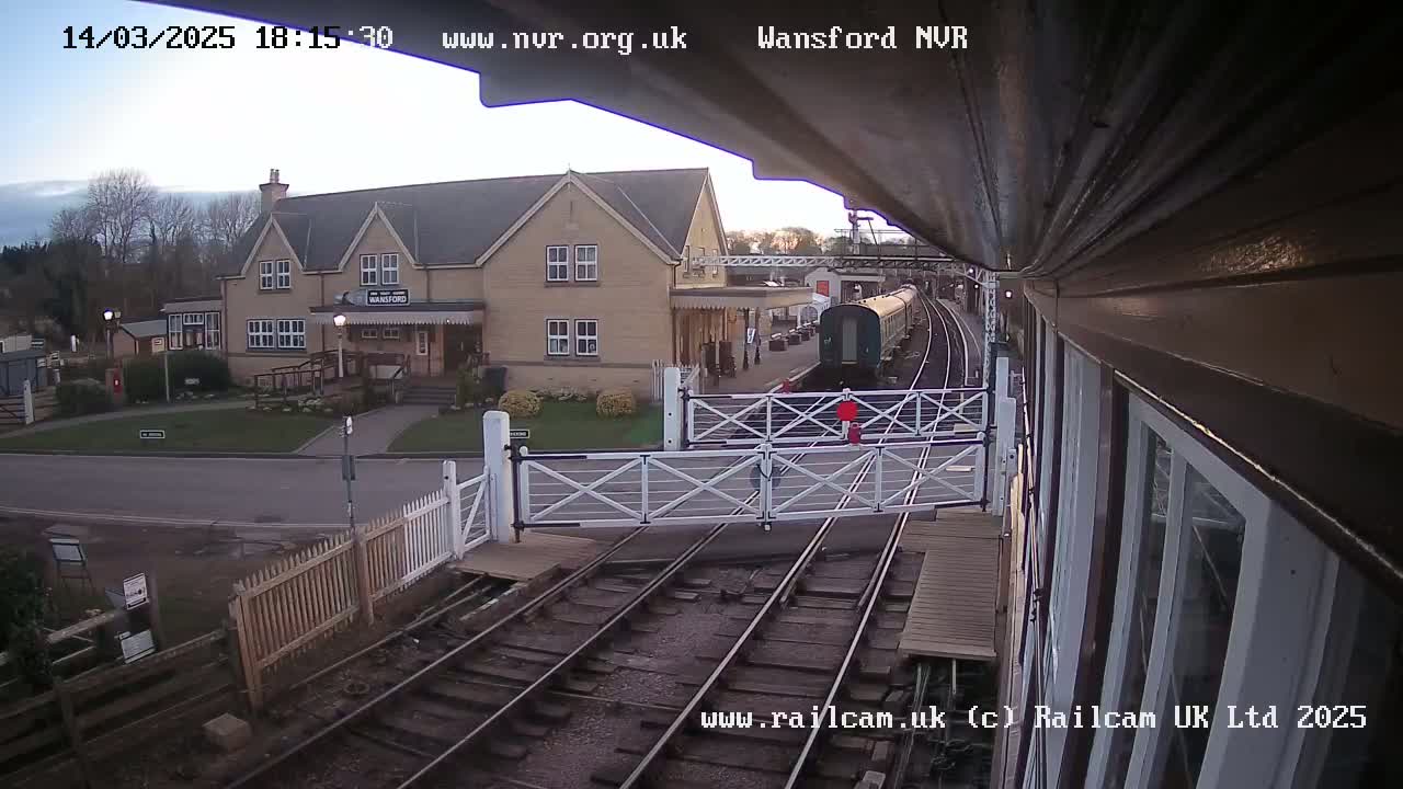 A train passes a railway station building on a partly cloudy day.