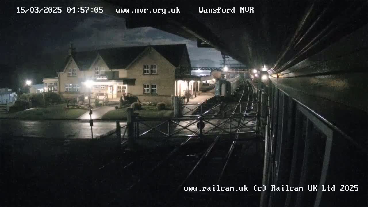 A nighttime view from a train shows a two-story building illuminated near a railway station under a partly cloudy sky.