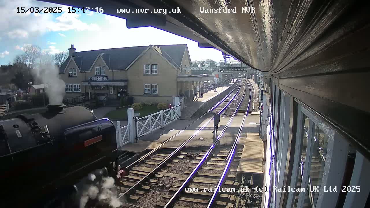 A steam train is departing from a station on a partly sunny day.