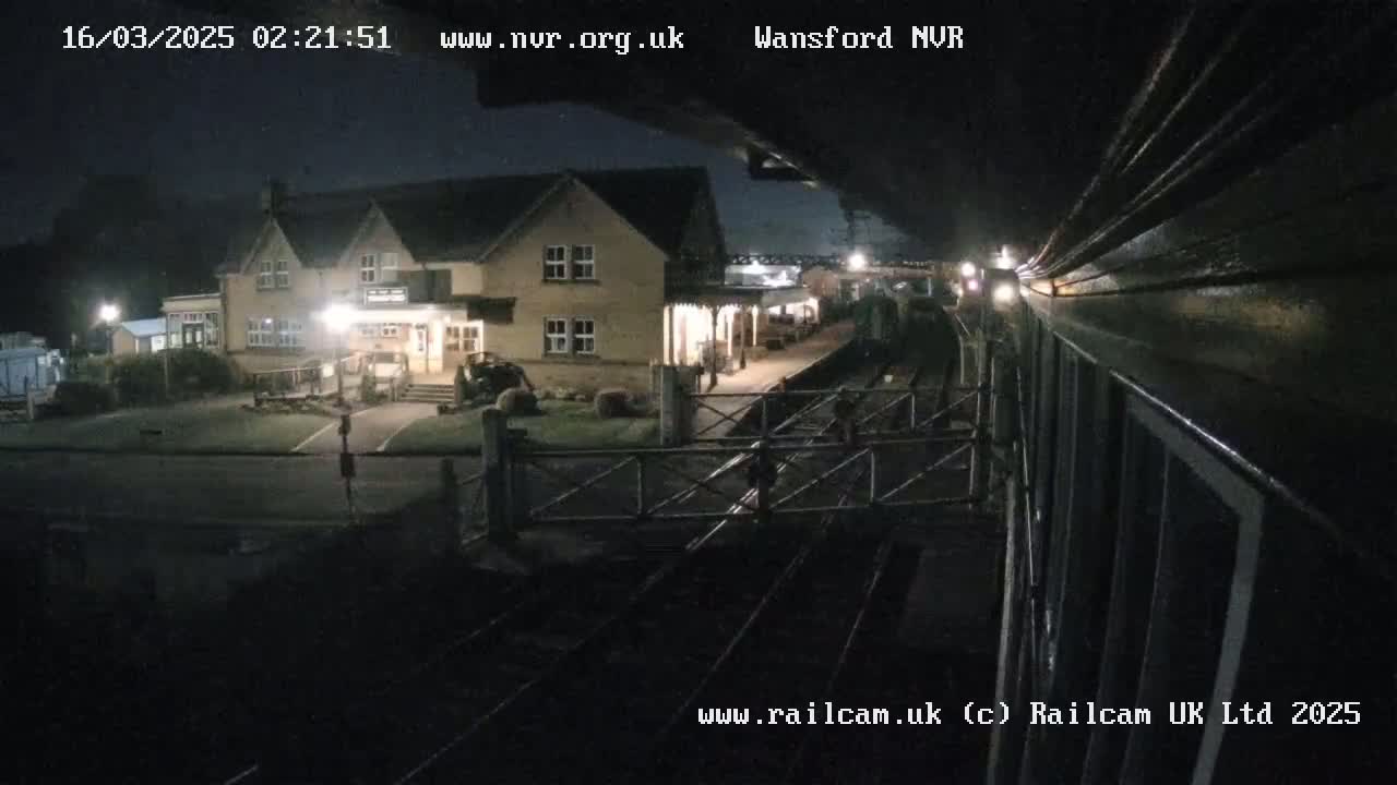 A nighttime view from a train shows a station building and railway tracks under a dark sky.