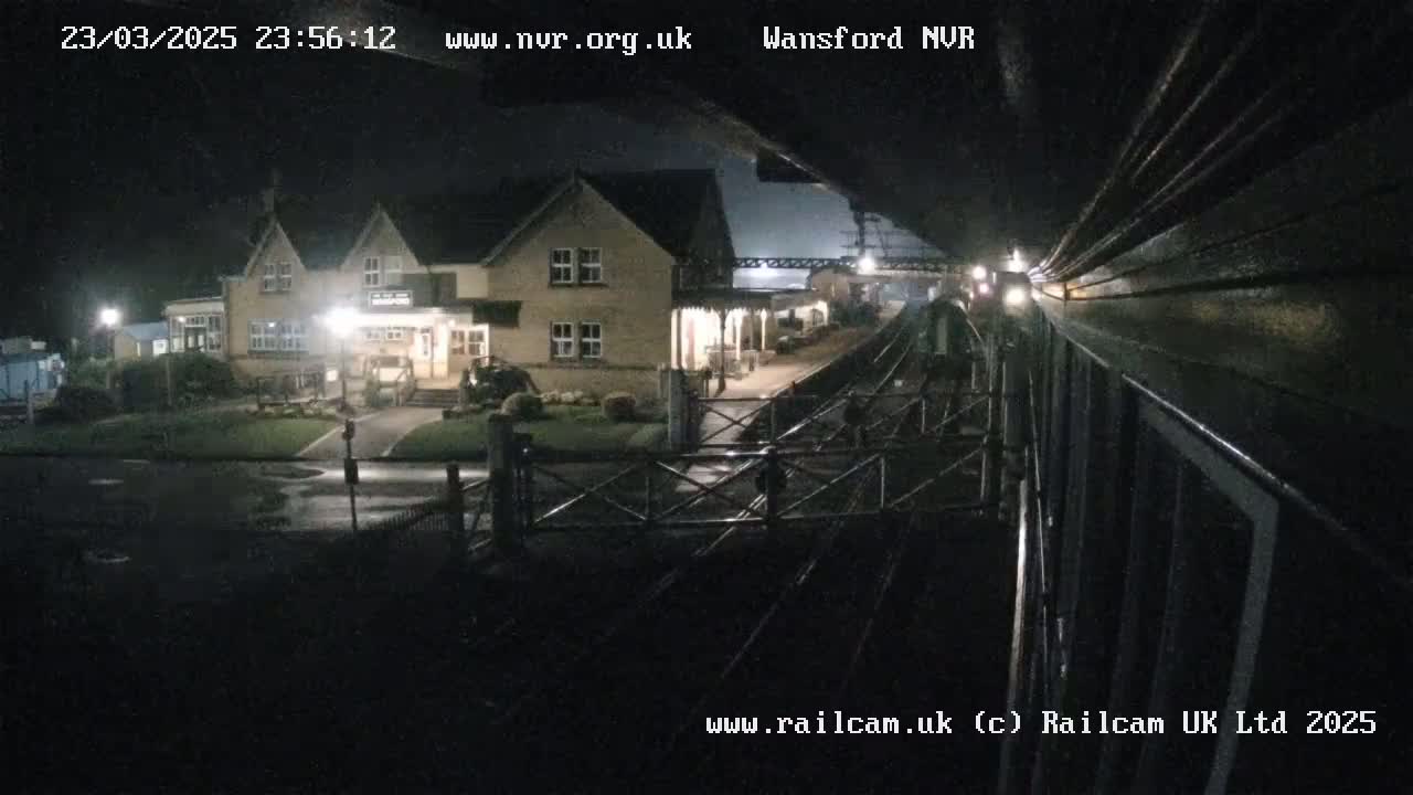 A nighttime view from a train shows a two-story building with lights on near a railway station.