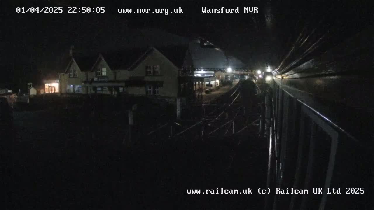 A nighttime view of a building and train tracks, with a vehicle visible in the distance.