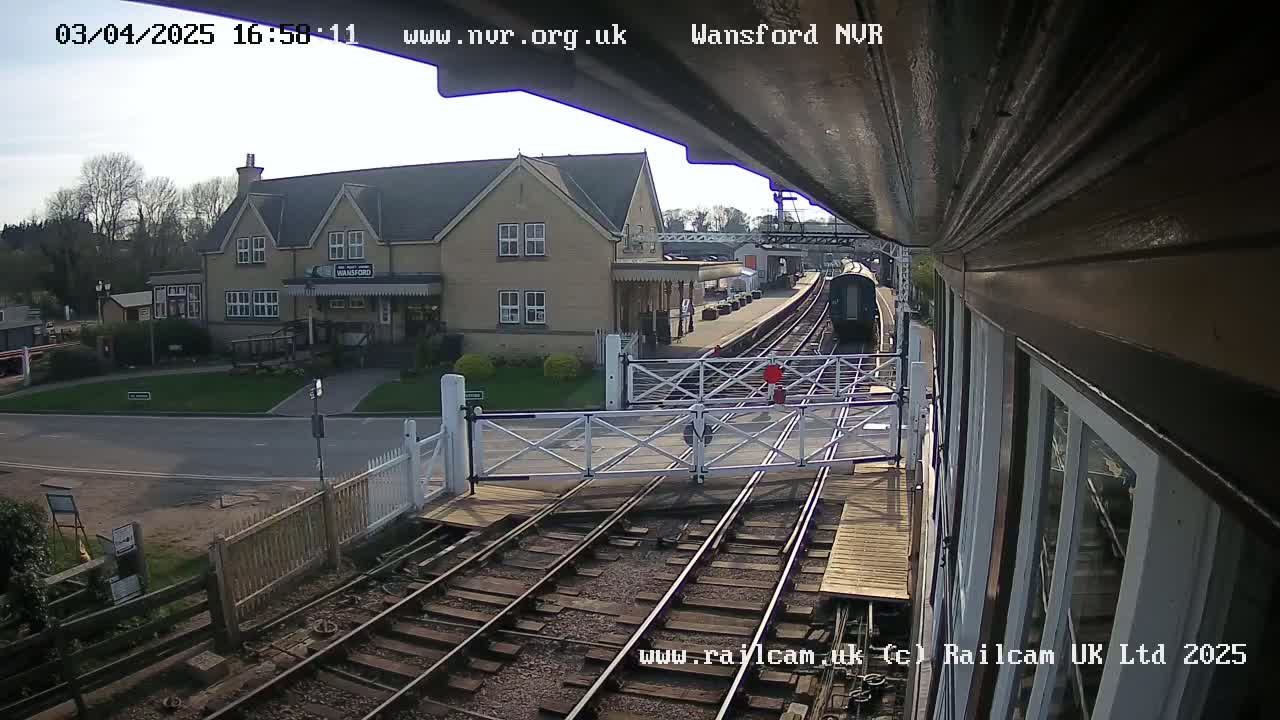 A train approaches a railway station on a sunny day, passing through a level crossing.