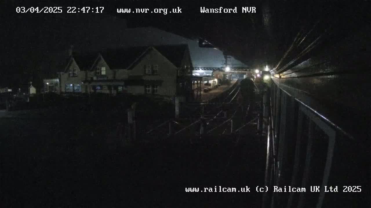 A nighttime view from a train shows a building and train tracks, under dark, possibly overcast conditions.