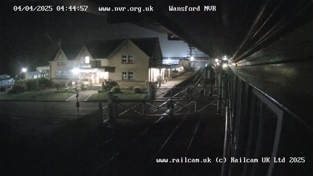 A nighttime view from a train shows a two-story building next to a train station with a level crossing gate.
