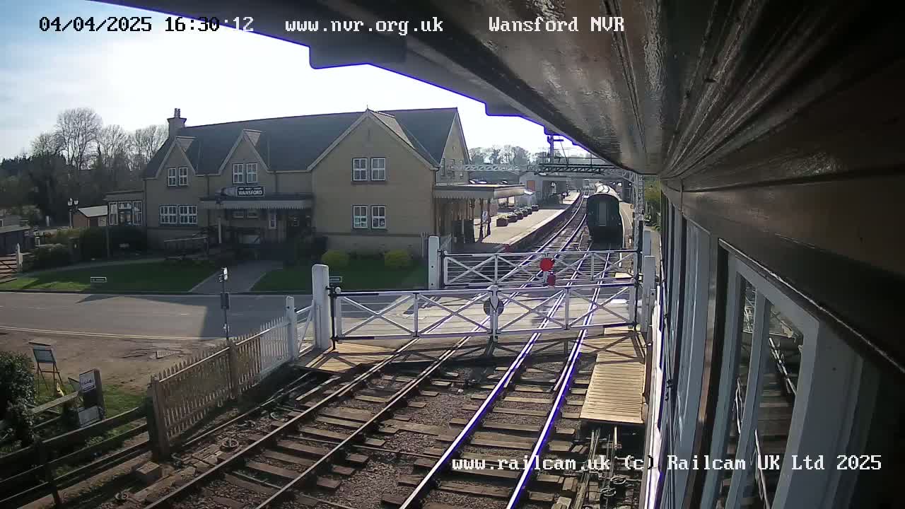 A train approaches a railway crossing in front of a station building on a sunny day.
