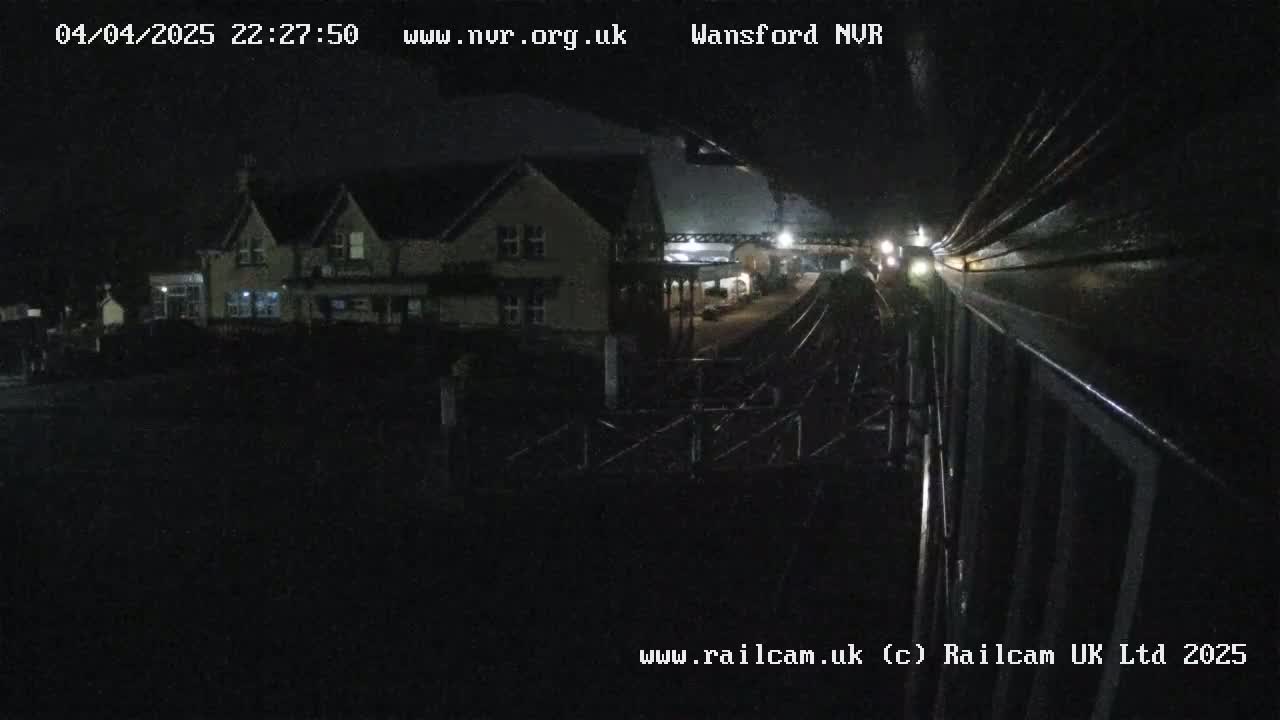 A nighttime view of a train station platform and a nearby building, under dark, clear skies.