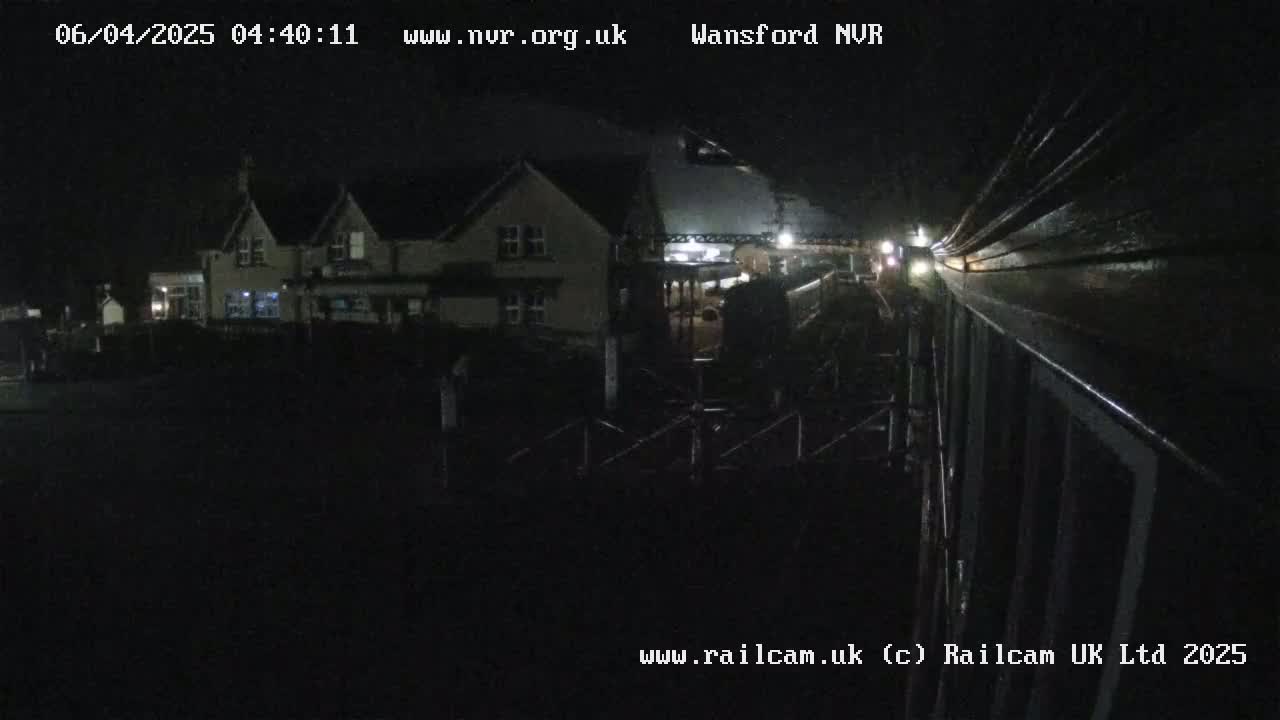 A nighttime view of a building near a train track, with a train partially visible in the distance.