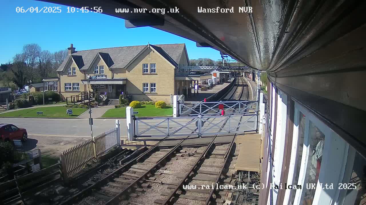 A sunny day at a train station with a two-story building and a level crossing, viewed from a train car.