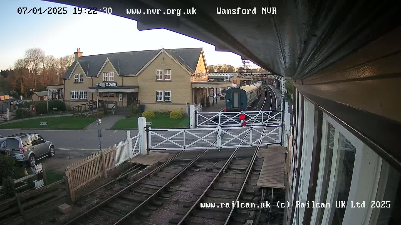 A train passes through a level crossing near a station building under a twilight sky.