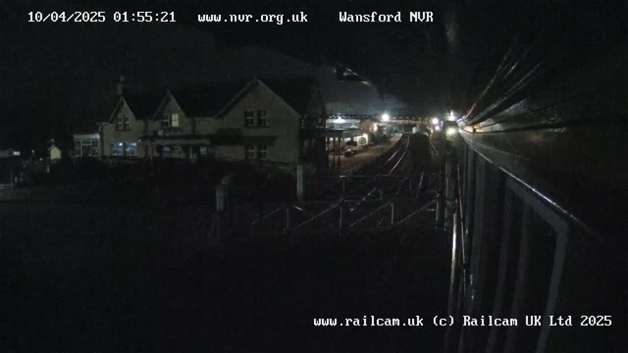 A nighttime view of a train passing a building near a railway track.