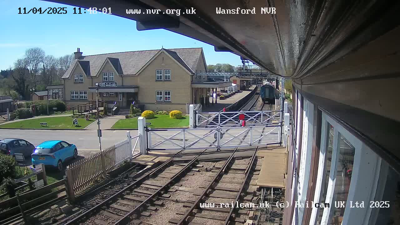 A train is arriving at a station on a sunny day, passing through a level crossing near a building.
