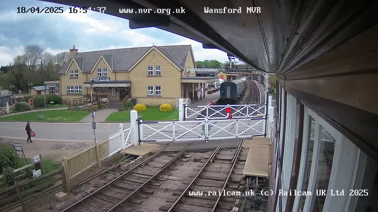 A train is stopped at a station on a partly cloudy day, with a person walking on the road nearby.