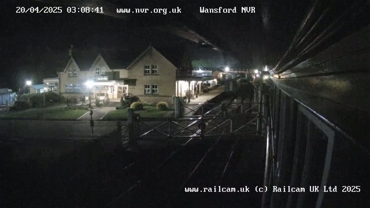 A nighttime view from a train shows a two-story building with lights on, a gated crossing, and train tracks.