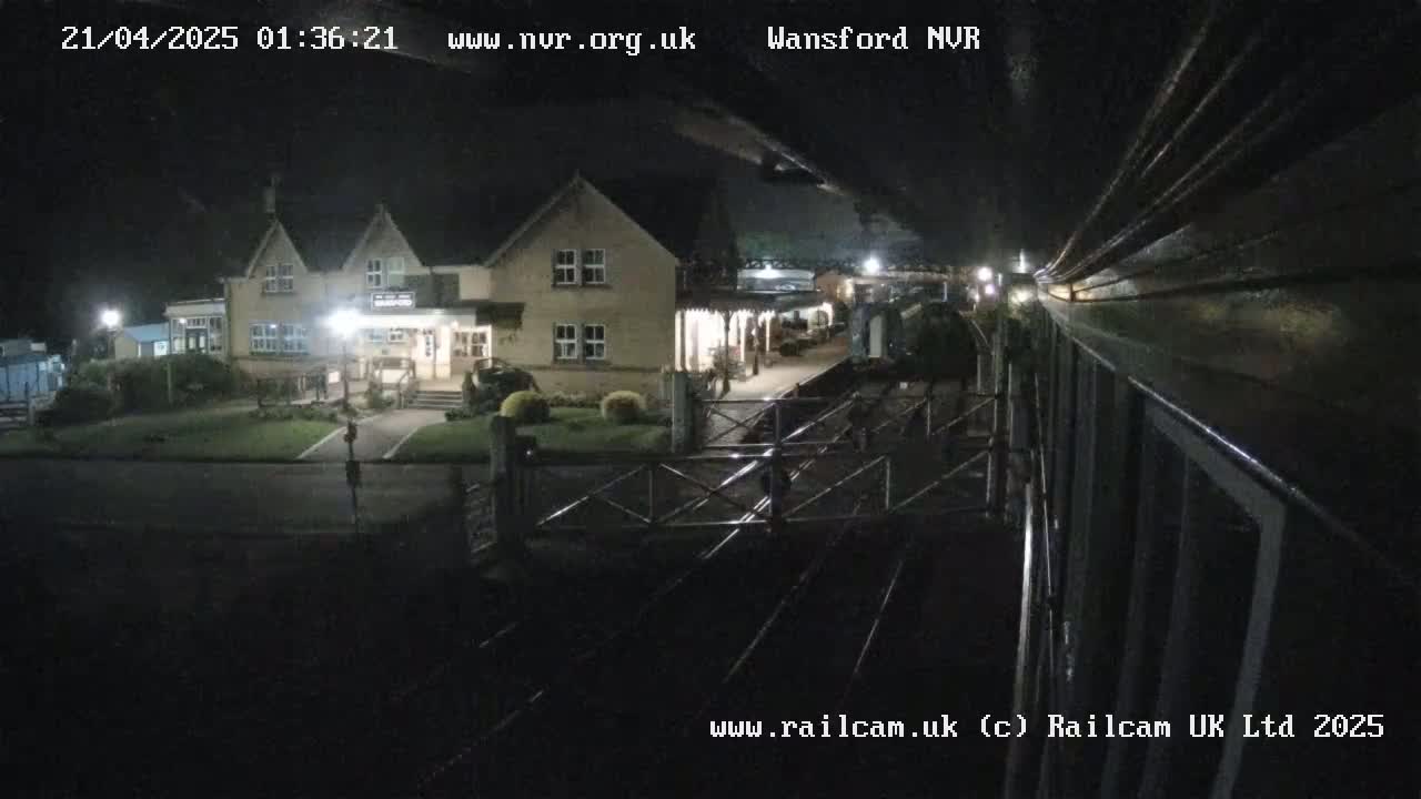 A nighttime view from a train shows a two-story building and a railway station platform.