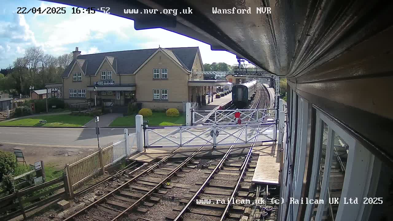 A train is arriving at a station on a sunny day, passing through a level crossing.