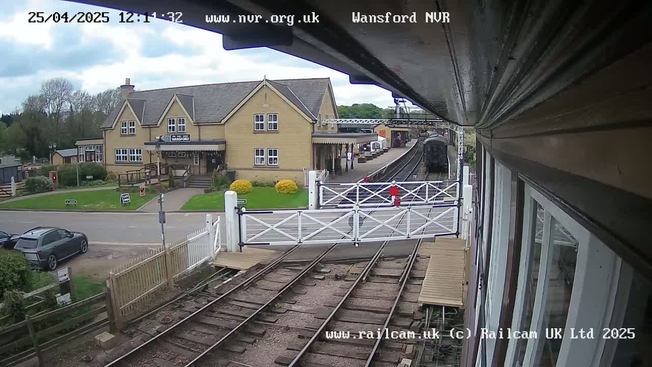 A train approaches a railway station building on a partly cloudy day.