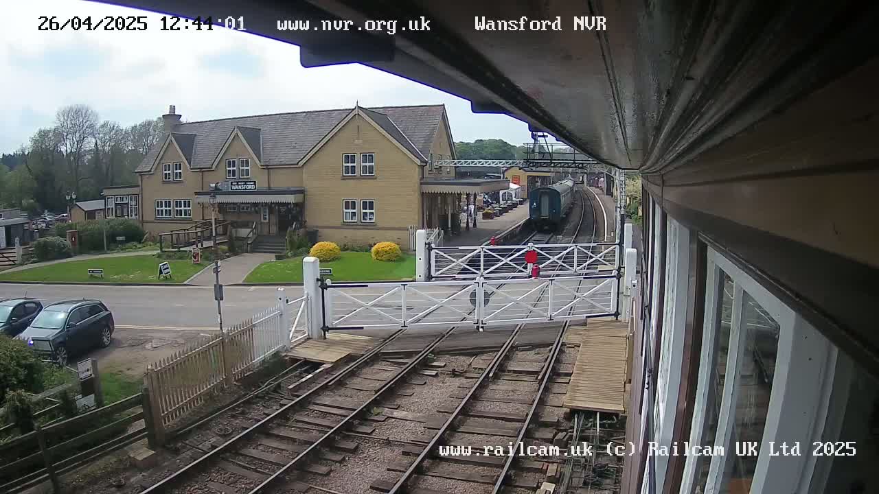 A train passes a station building on a partly cloudy day.