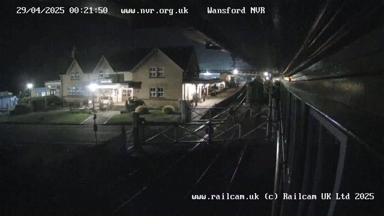 A nighttime view from a train shows a station building illuminated under a dark sky.