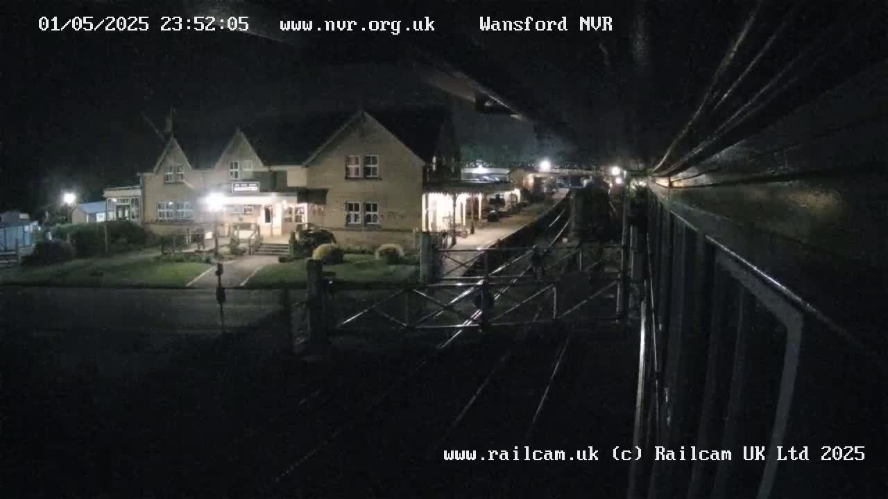 A nighttime view from a train shows a two-story building near a train station platform and tracks.