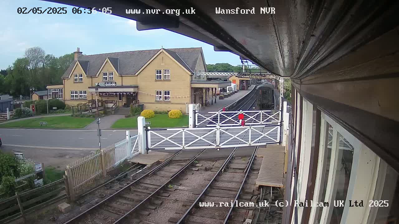 A train approaches a station building under partly cloudy skies.