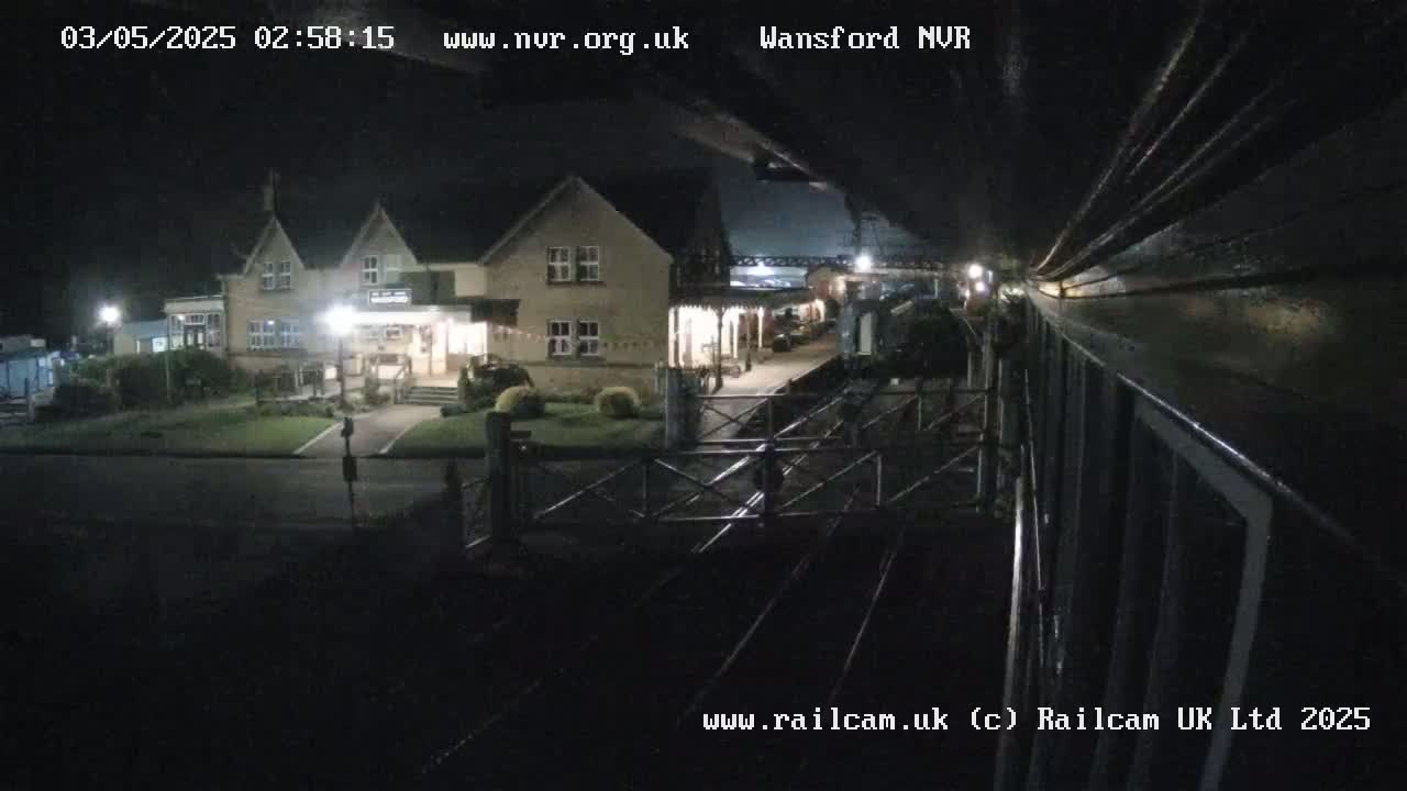 A nighttime view from a train shows a building with lights on and a train station platform.