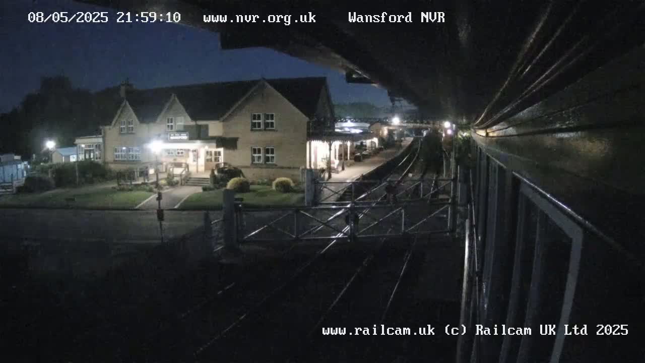 A nighttime view from a train shows a two-story building near a train station with a level crossing.