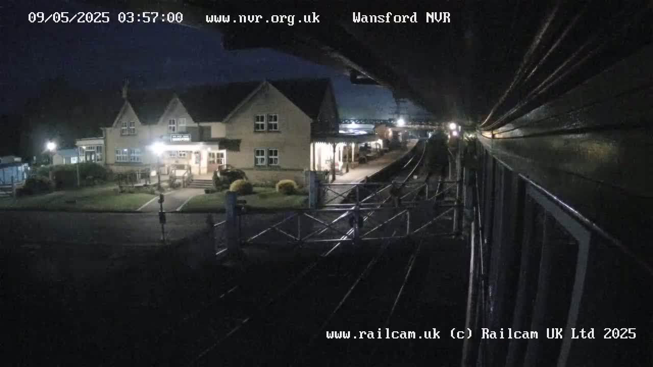 A nighttime view from a train shows a two-story building next to a train station platform and tracks.
