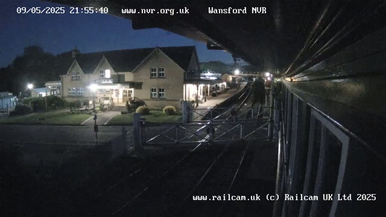 A nighttime view from a train shows a two-story building next to a train station with railway tracks in the foreground.