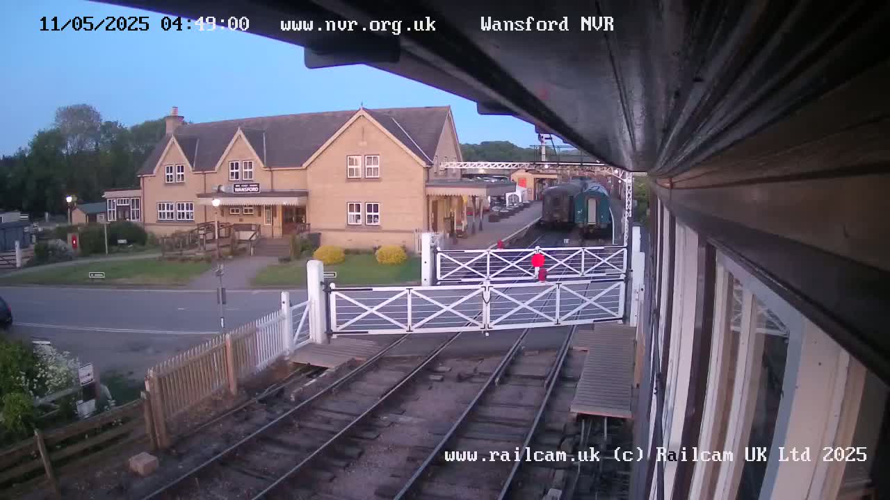 A train is arriving at a railway station near a light-colored building under a twilight sky.