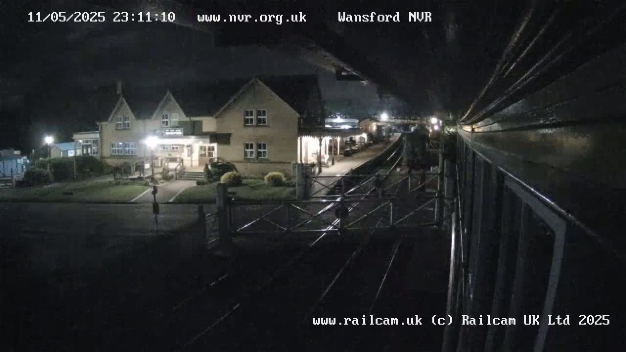 A nighttime view from a train shows a two-story building next to a train station platform and railway tracks.