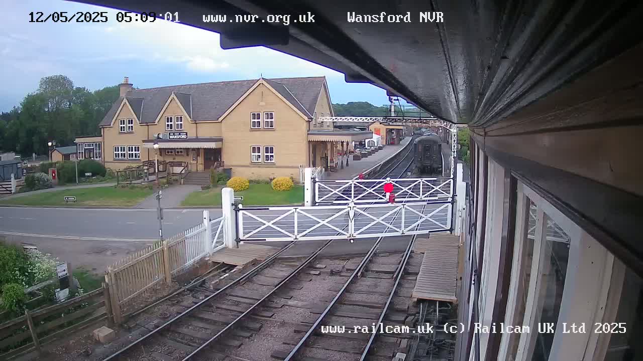 A train approaches a railway crossing in front of a two-story building on an overcast day.