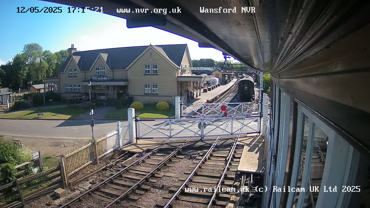 A train approaches a station on a sunny day, passing through a level crossing.