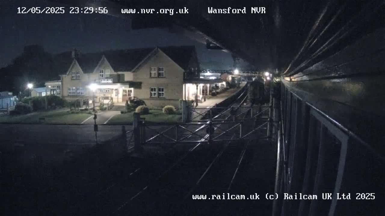 A nighttime view from a train shows a two-story building near a train station platform and tracks.