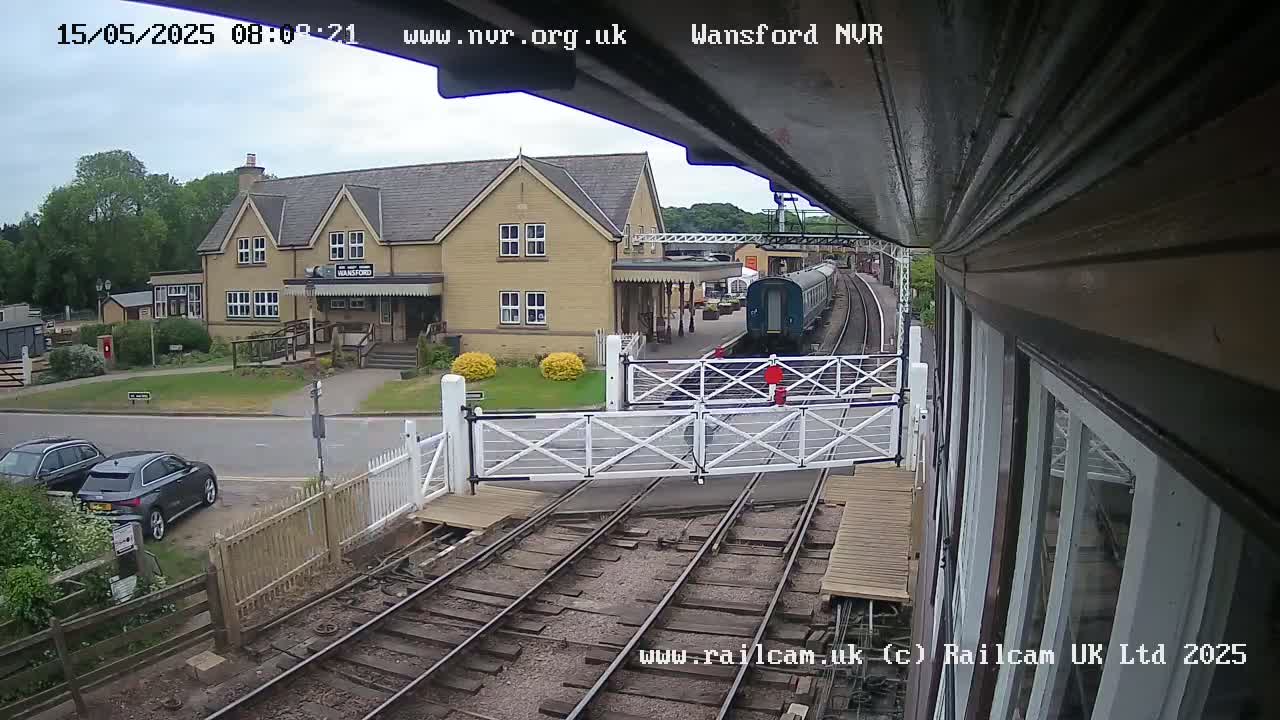A train is stopped at a railway station next to a two-story building under a partly cloudy sky.