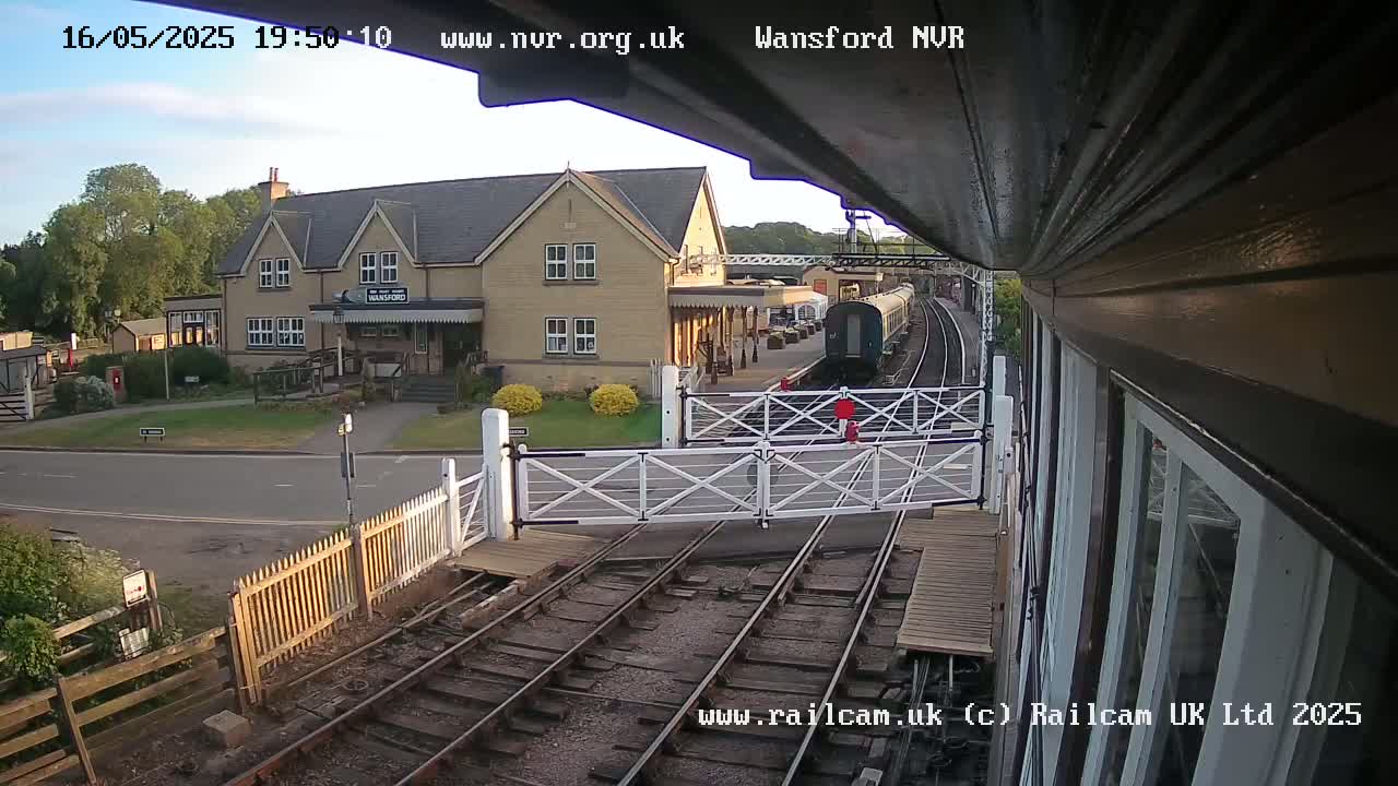 A train passes a railway station building under a partly cloudy evening sky.