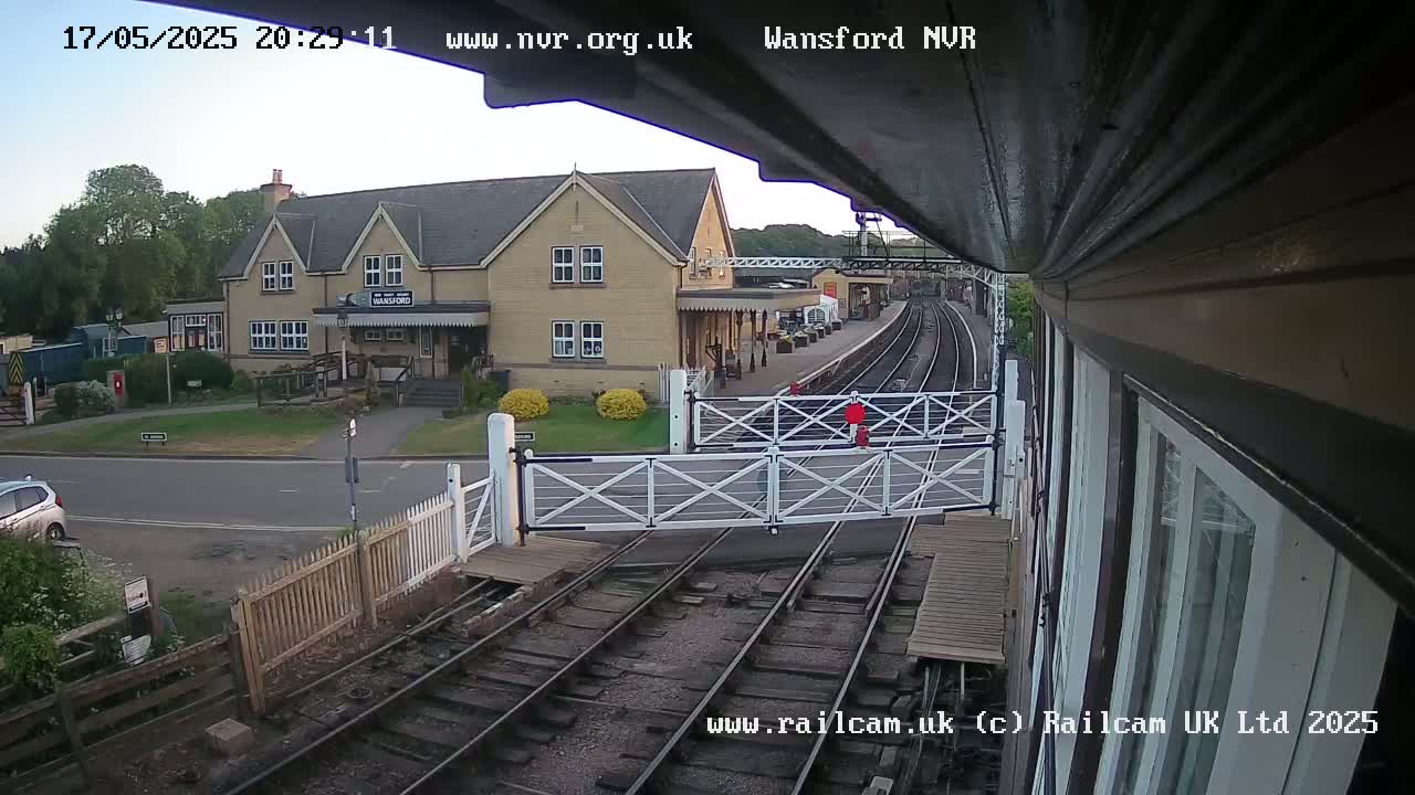 A train station with a two-story building under a twilight sky, featuring a level crossing gate and train tracks.