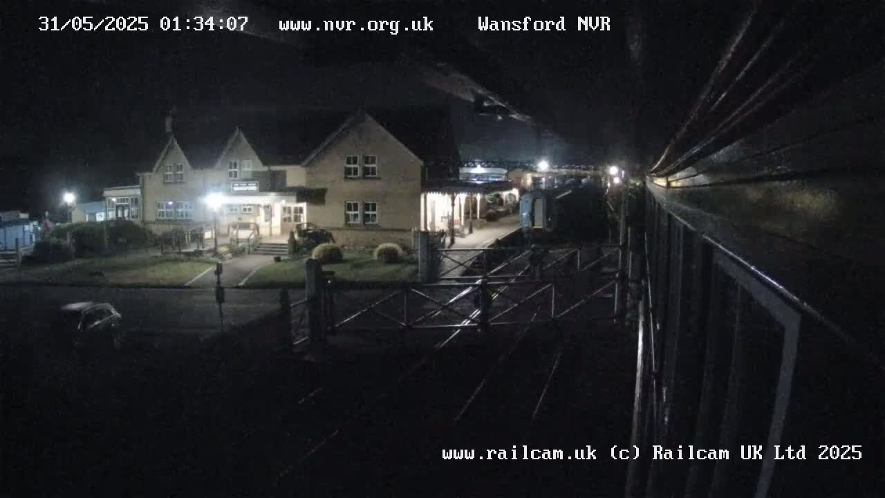 A nighttime view of a train station with a building and a vehicle in the parking lot under a dark sky.