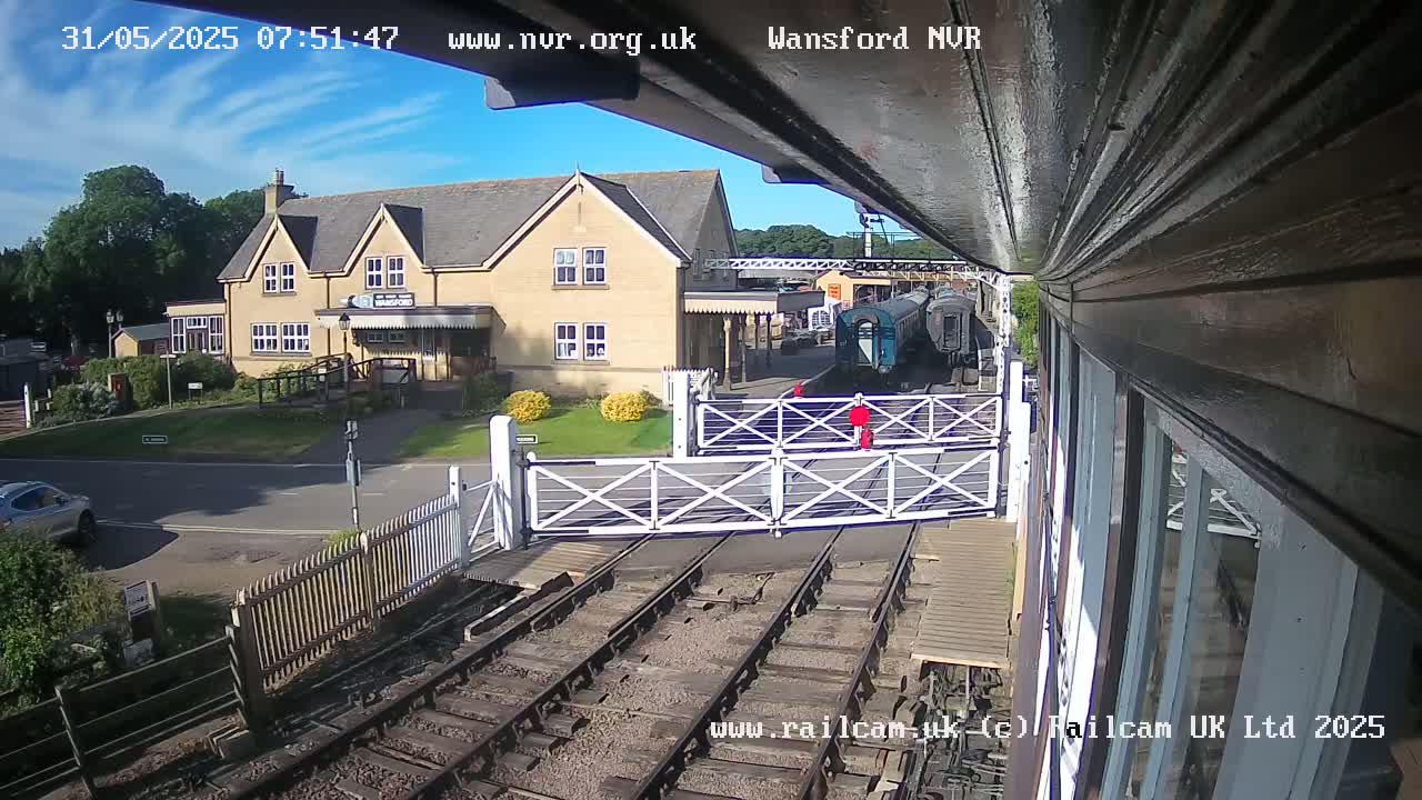 A train is stopped at a railway crossing near a light-yellow building on a sunny day.