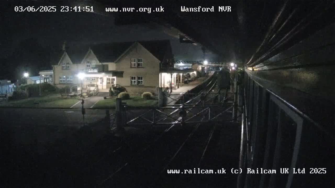 A nighttime view of a train station building and railway tracks, illuminated by artificial lights.