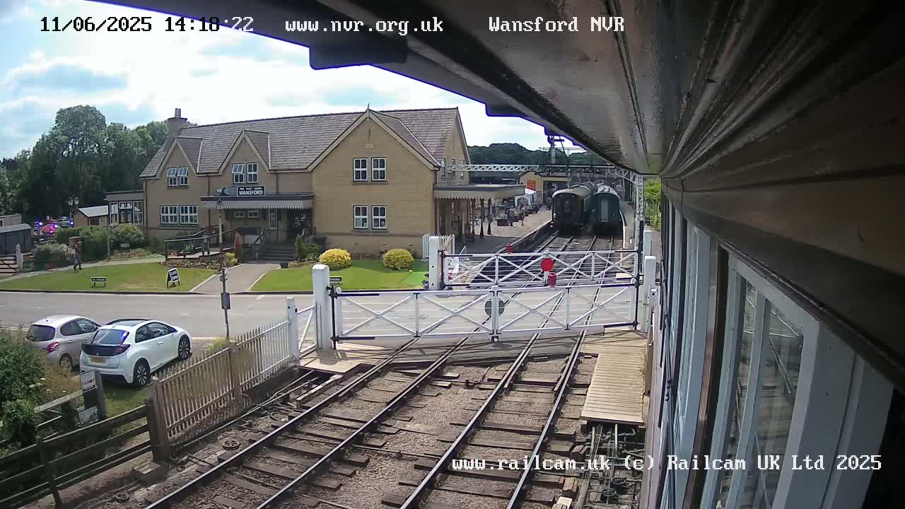 A train is approaching a level crossing near a stone building on a sunny day.