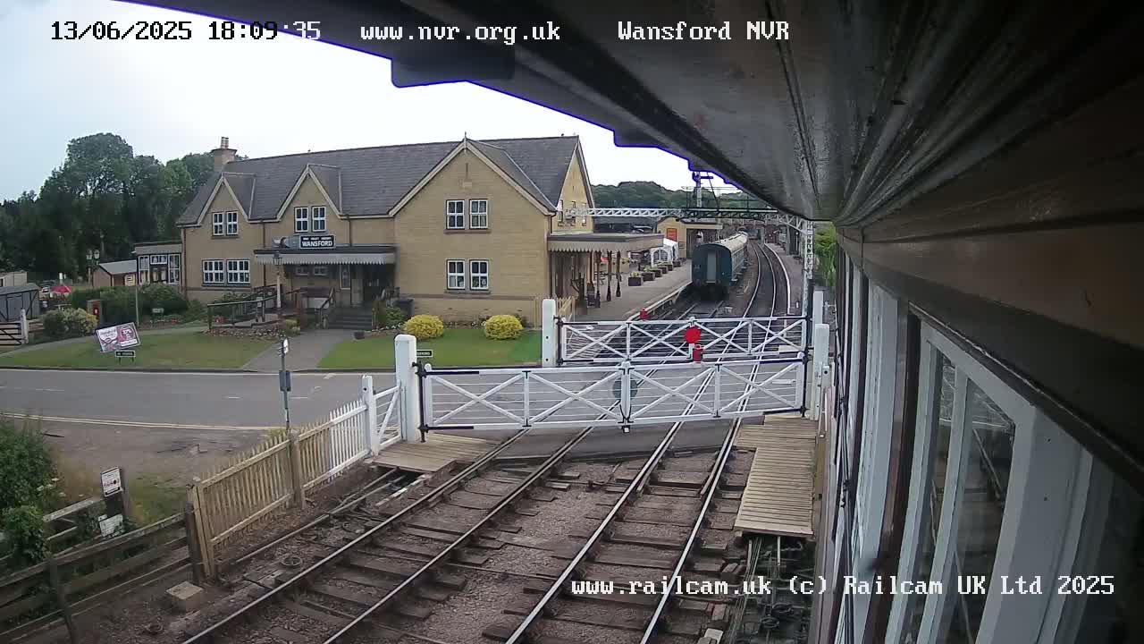 A train is passing a station on a mostly sunny day, with a two-story building visible in the background.