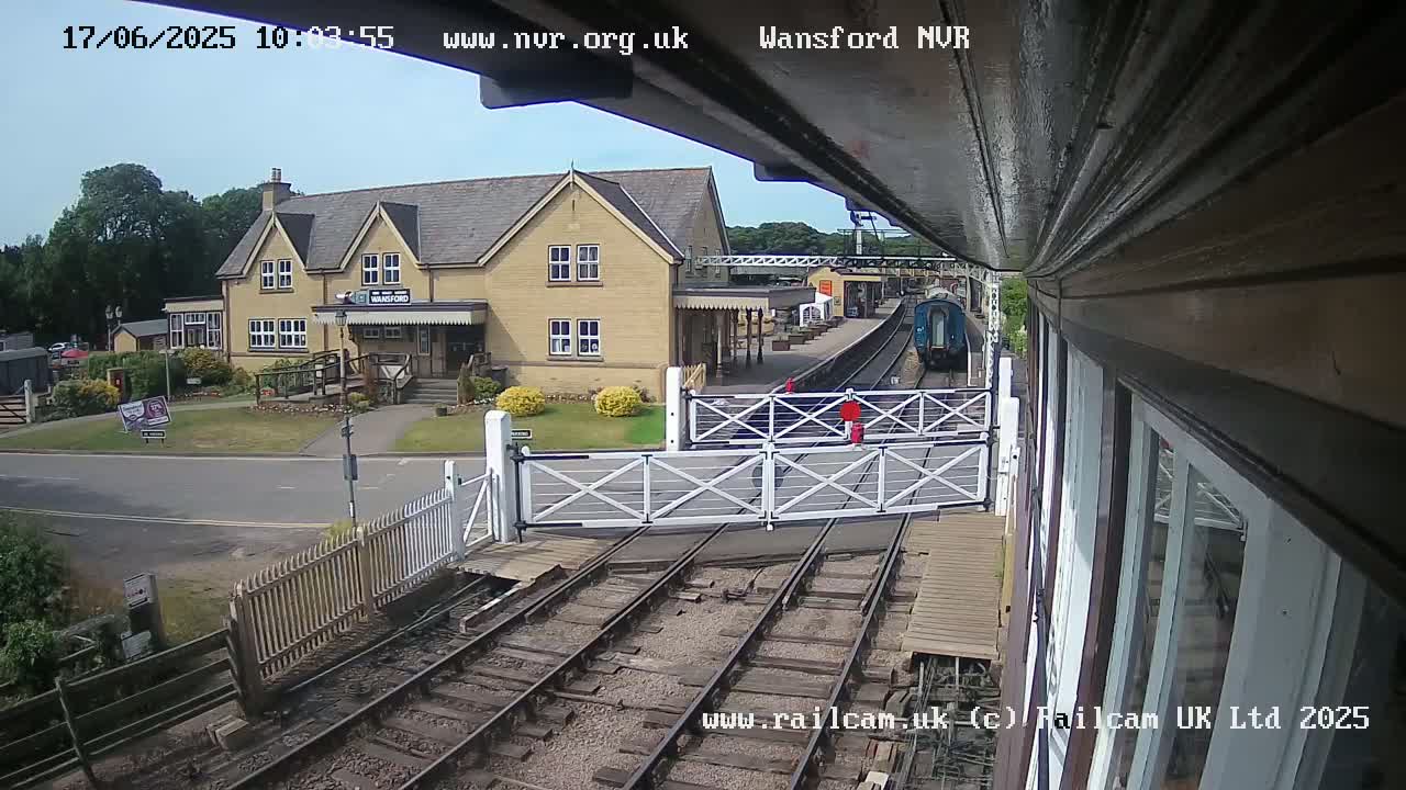 A train approaches a railway station on a sunny day, passing through a level crossing.